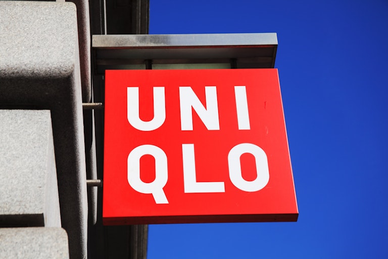 Image showing bright red Uniqlo brand sign against a blue sky and brick wall